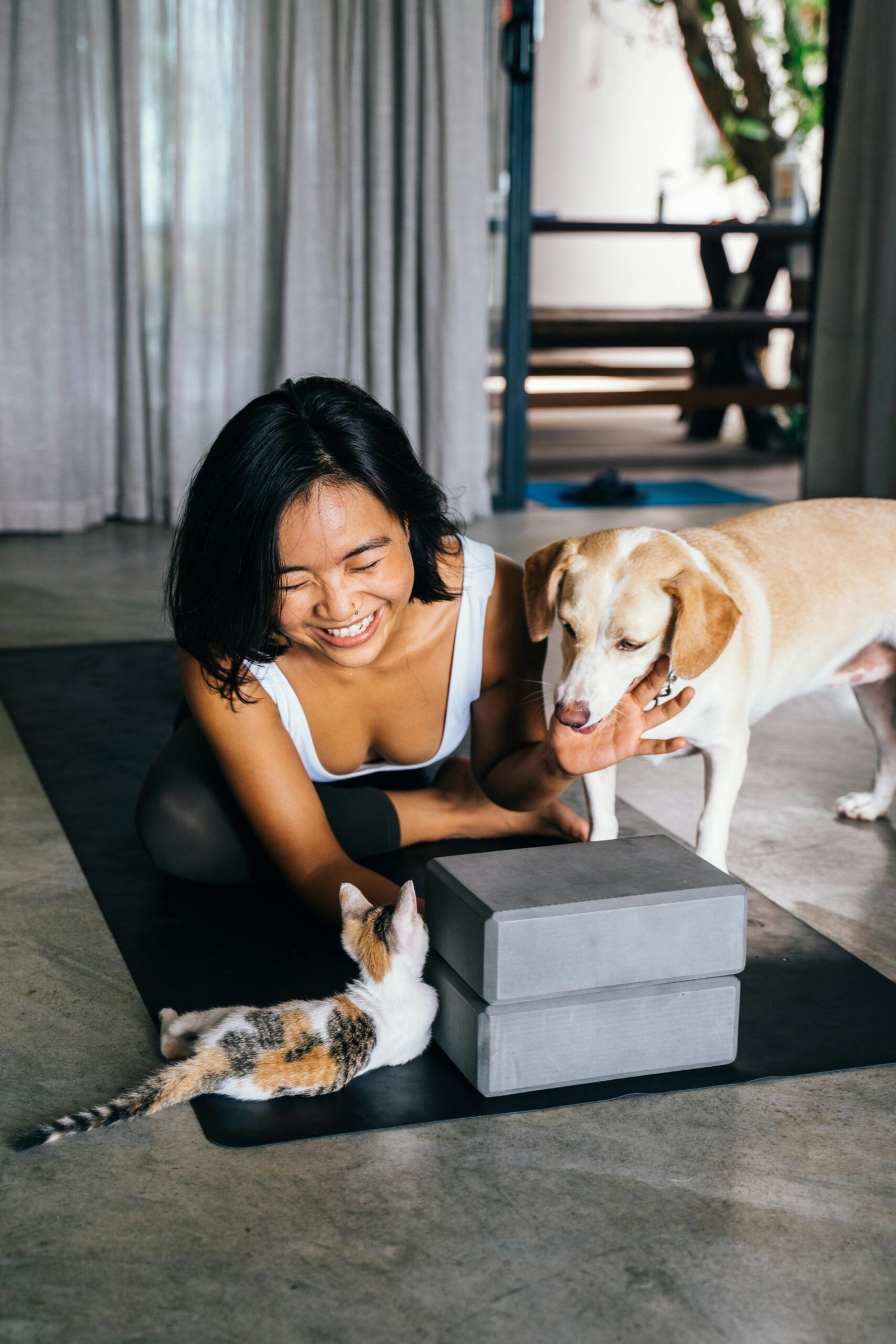 Smiling woman with dog and cat relaxing on a yoga mat indoors.